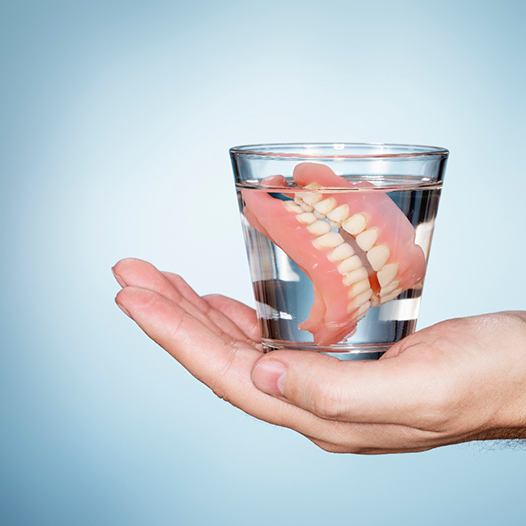 Hand holding a glass of water with dentures