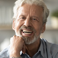 Man with dentures holding hand to chin smiling