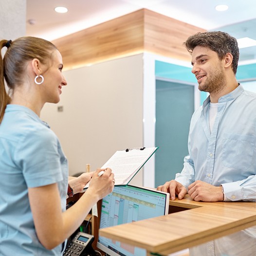 young male dental patient talking to front desk person 