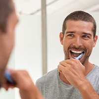 Man smiling while brushing his teeth in bathroom