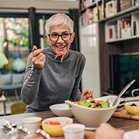 Woman with black glasses smiling while eating with friend