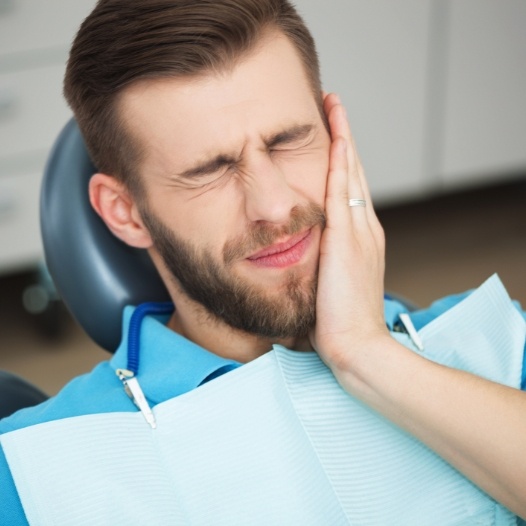 Man in need of tooth extraction holding cheek in pain