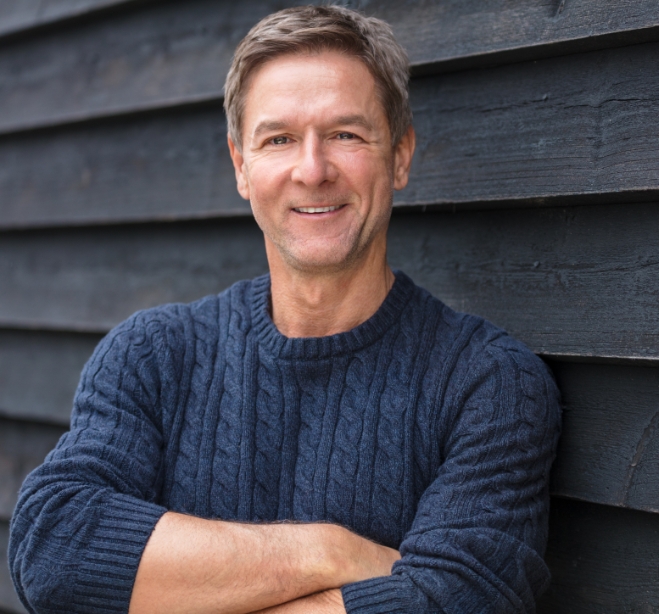 Smiling man in blue sweater standing with arms crossed