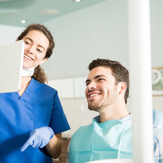 dental assistant showing smiling patient someone on tablet 