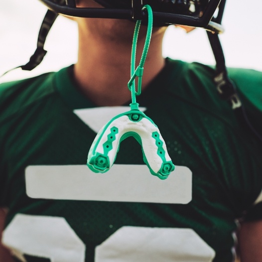 Teen with athletic mouthguard hanging from football helmet