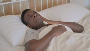Man in bed holding face in pain. 